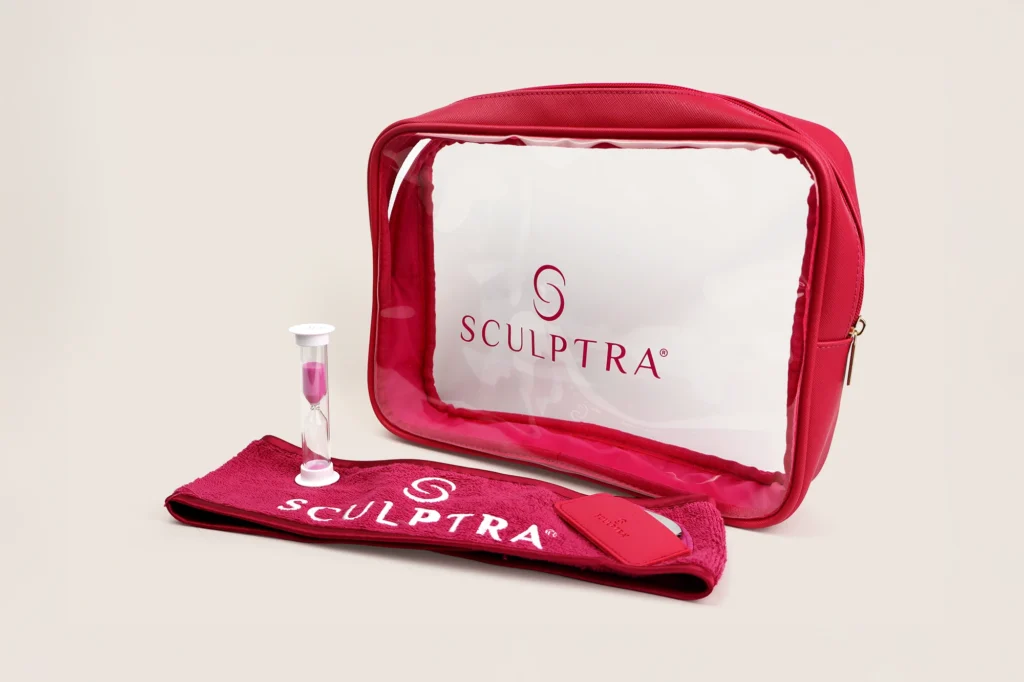 A red cosmetic bag with a clear front, containing an hourglass and a red towel featuring the "Sculptra" logo.