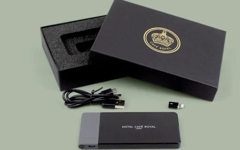 A smartphone power bank with a USB charging cable and a small adapter, placed next to a black box featuring a 