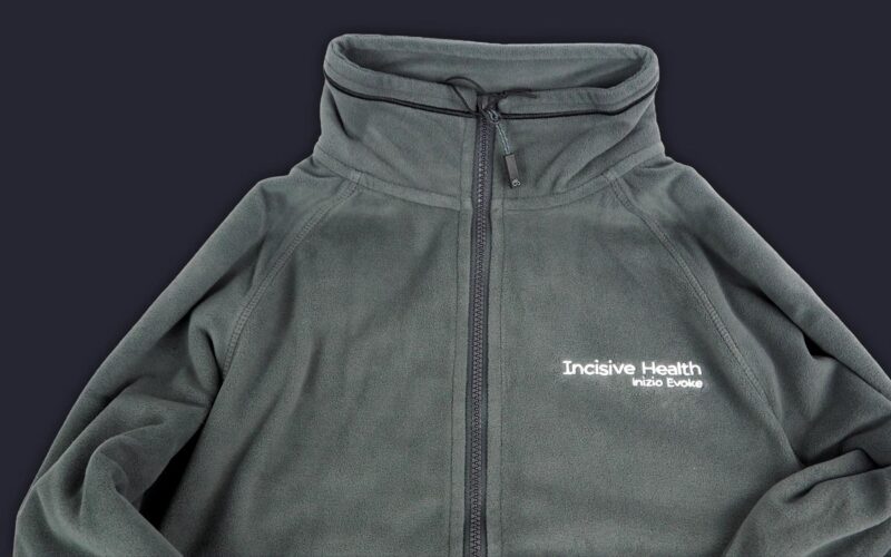 A dark gray fleece jacket with a high collar and a zip closure, featuring the text 