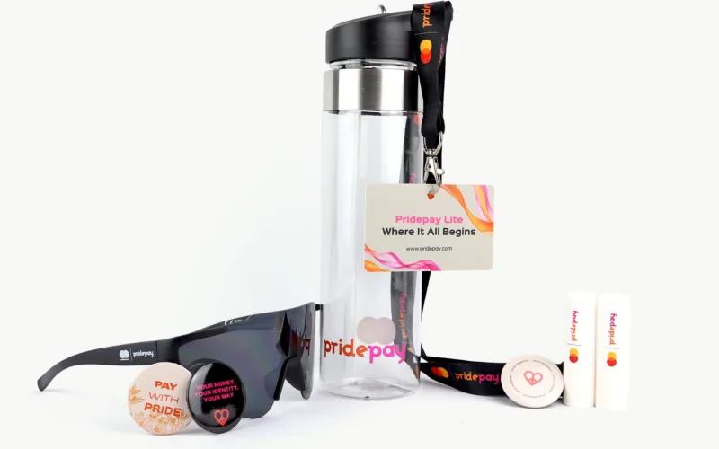 A collection of promotional items including sunglasses, a water bottle, a lanyard with a card, lip balm, and buttons. The items feature the 