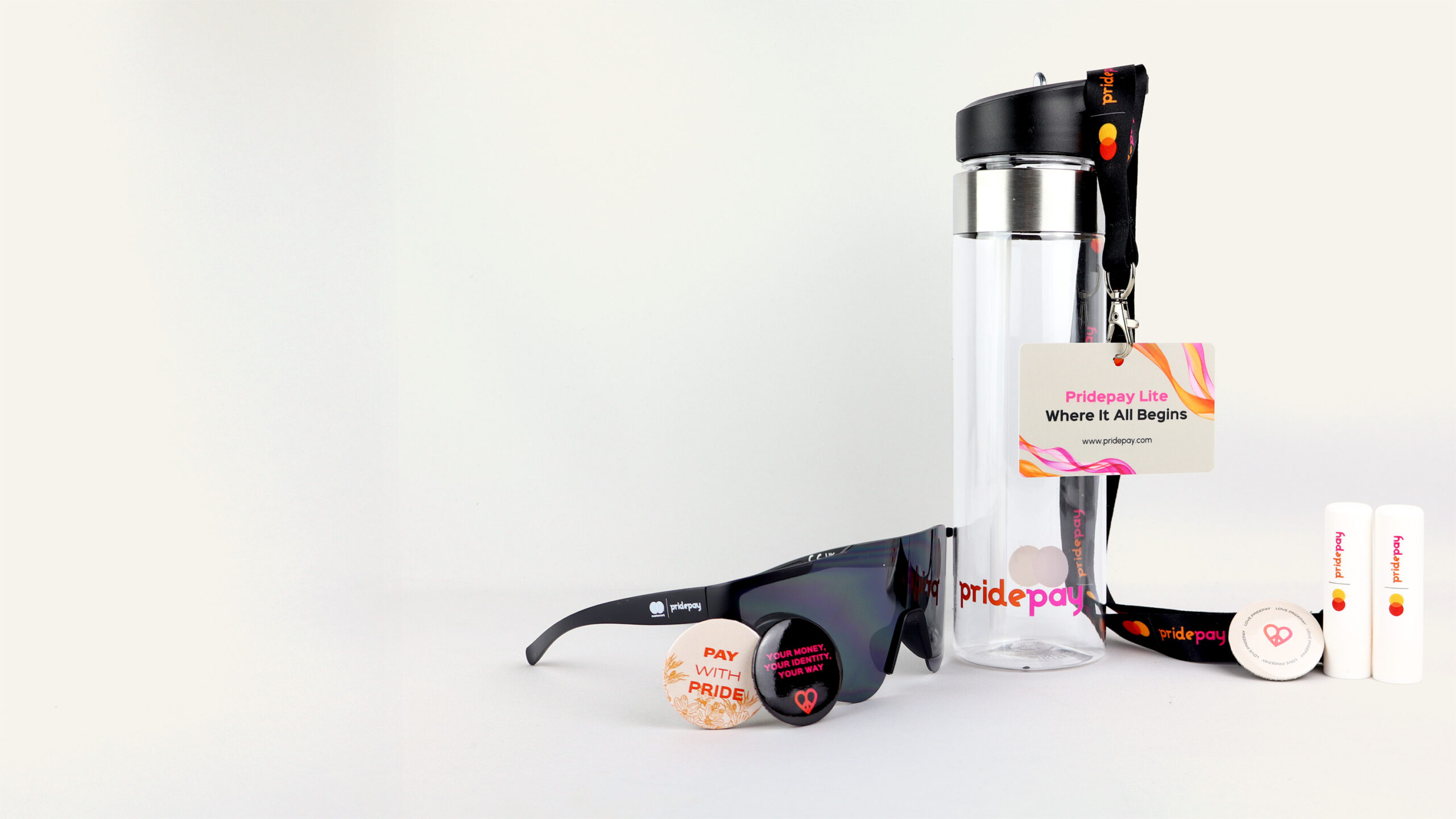 The image features a collection of promotional items: a water bottle, sunglasses, two pins, a lanyard with an ID card, and two lip balms, all branded with PridePay.