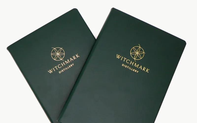 Two green notebooks with the gold logo and text 