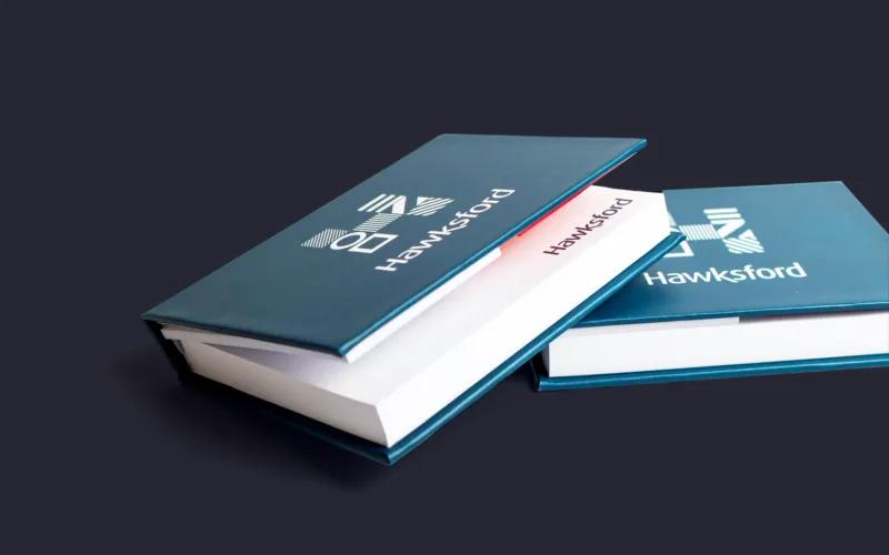 Two hardcover books with a dark blue cover, featuring the logo and name 