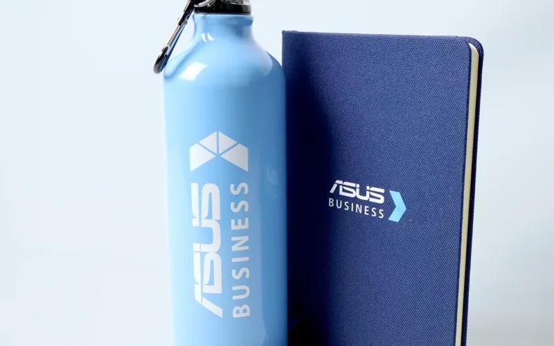 A light blue water bottle, a blue notebook, and two blue pens, all branded with 