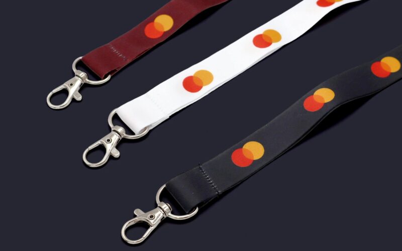 Three lanyards in different colors (maroon, white, and black) featuring circular patterns in red and yellow, with metal clips on the ends.
