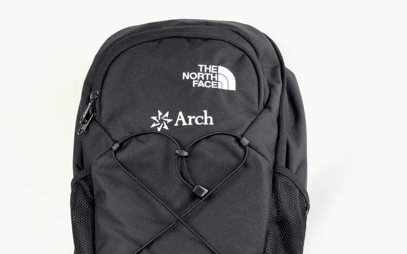A black backpack featuring logos from The North Face and Arch, with elastic cords shaped like a heart.
