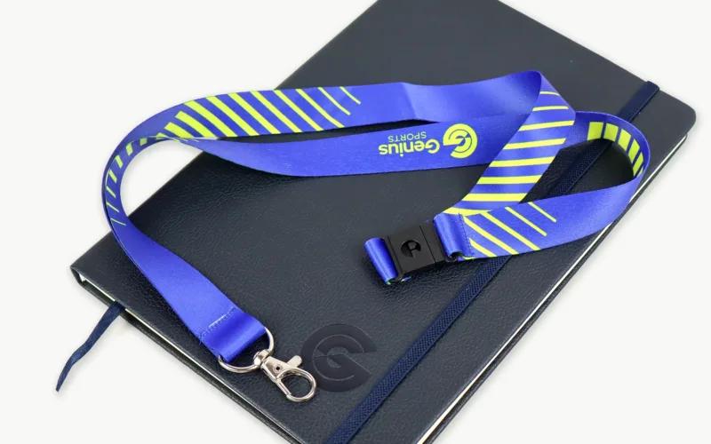 A blue lanyard with green stripes is placed on top of a black notebook.