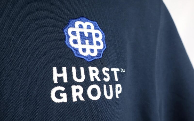 The image features an embroidered logo on a dark navy fabric, displaying the text 