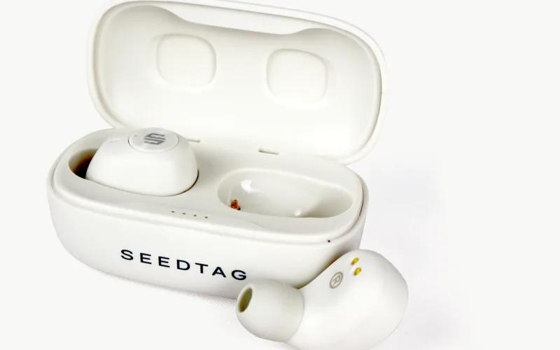 A pair of white wireless earbuds in their charging case, with one earbud placed outside the case.