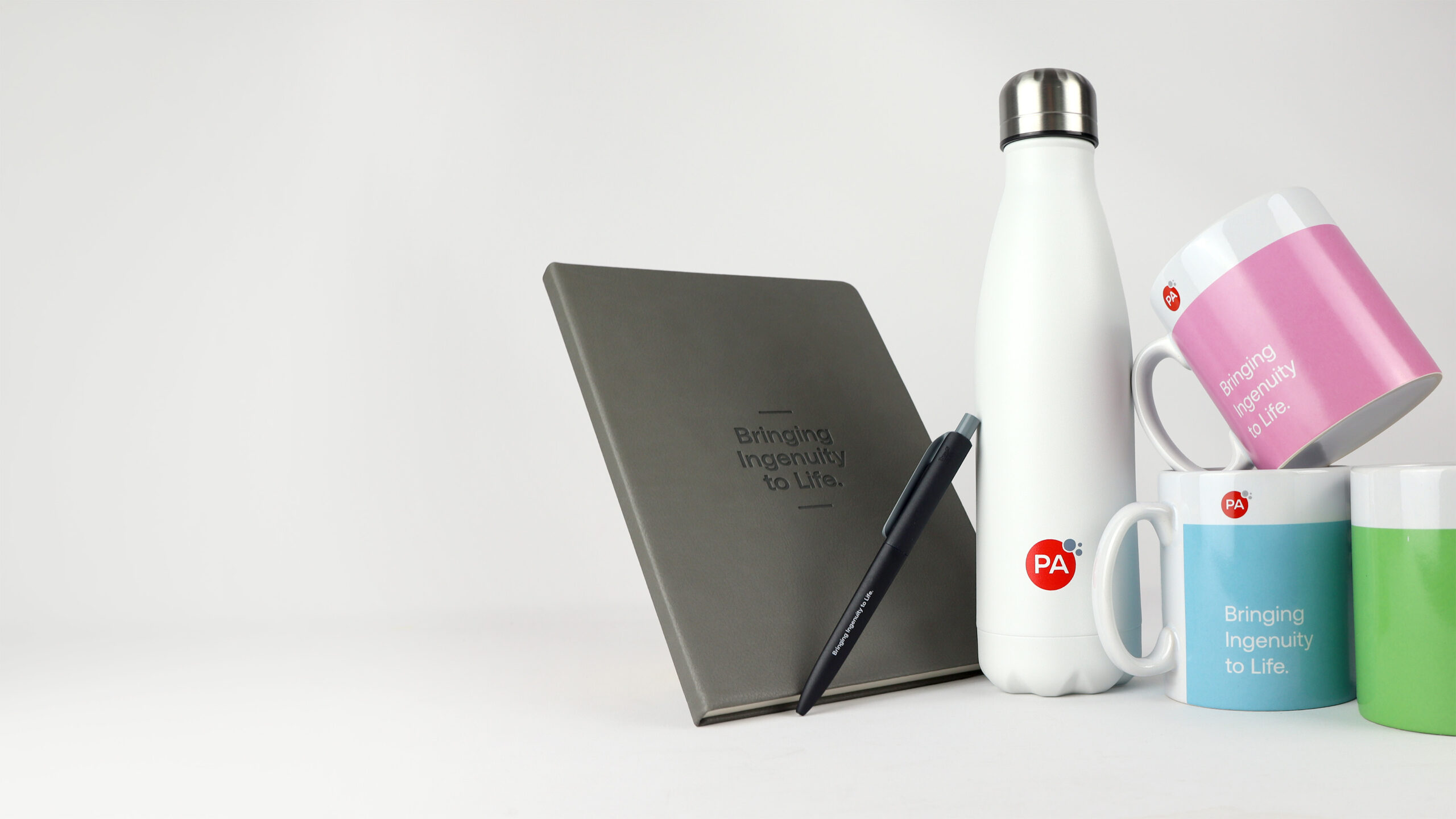 A notebook, a pen, a white insulated water bottle, and three colorful mugs, each featuring the phrase 
