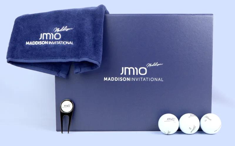 A navy towel, a golf tee, three white golf balls, and a blue box with 