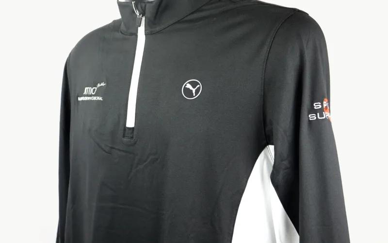A black and white athletic long-sleeve pullover shirt with a quarter-zip collar and logos on the chest and arm.