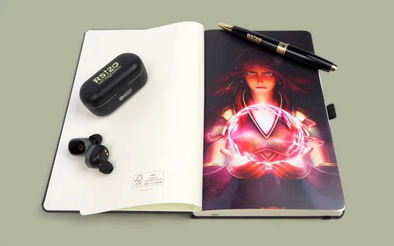 A notebook featuring an illustration of a character with magical energy, a pair of black wireless earbuds, and their charging case, alongside a pen.