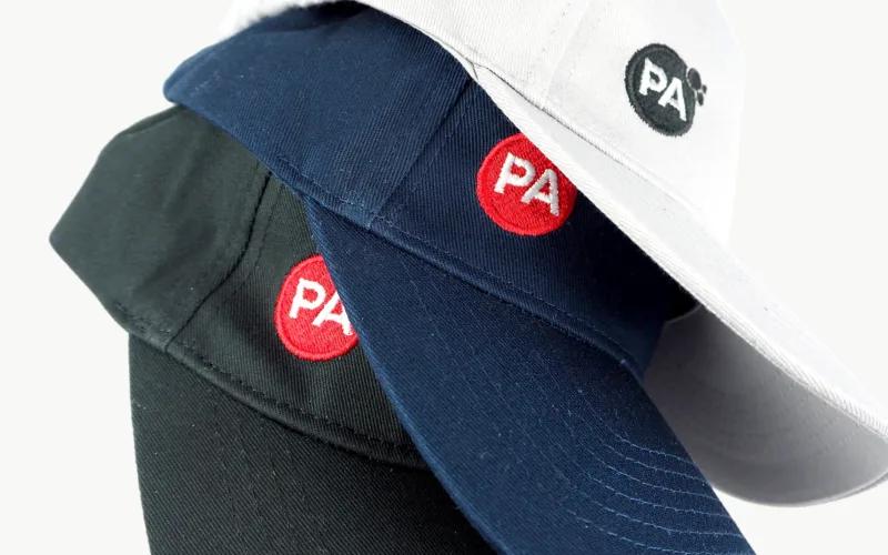 Three baseball caps in different colors (black, navy, and white) with the letters 