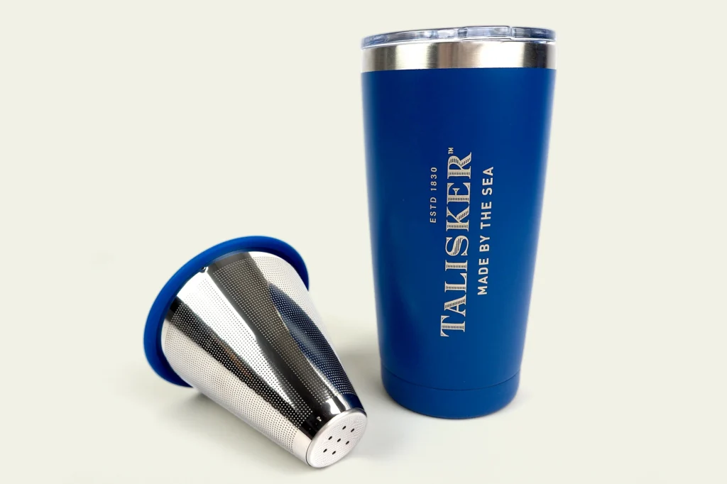 A blue insulated tumbler with a stainless steel mesh tea infuser beside it.