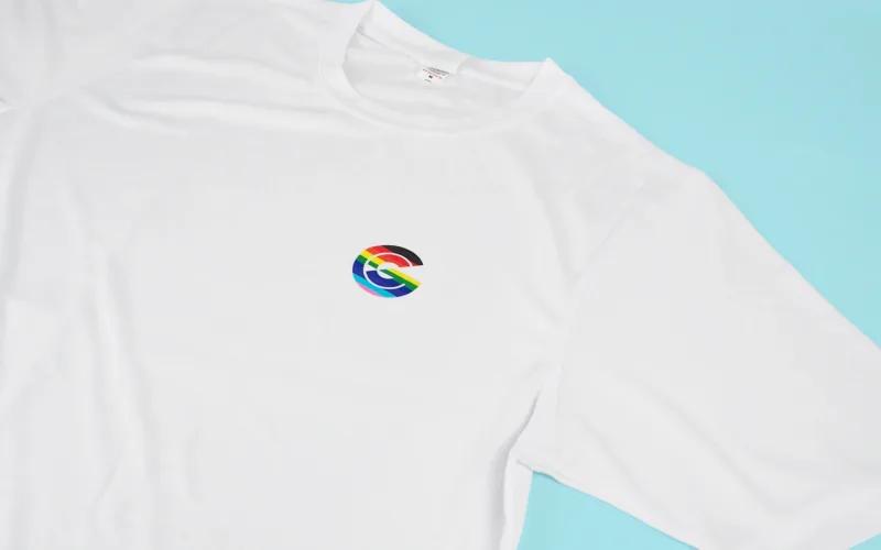 A white t-shirt featuring a colorful logo on the left chest area, laid on a light blue background.